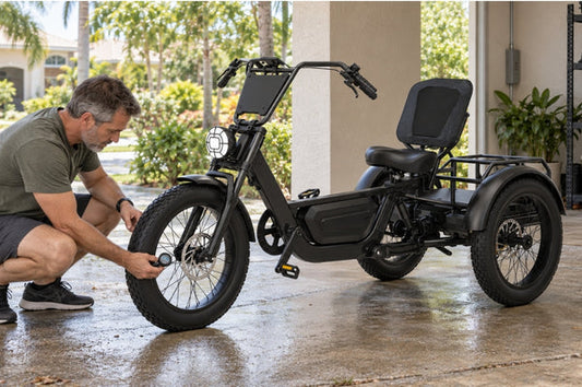 An owner performs electric trike maintenance in Florida by checking the front tire of the FlekTrike Pro All-Terrain Tilting eTrike in a shaded residential carport.