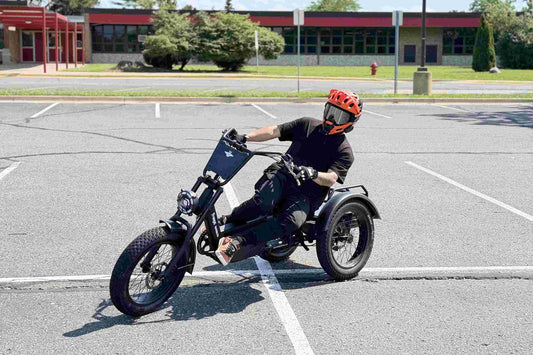 Helmeted rider cornering on the FlekTrike leaning electric trike within an open paved parking lot.