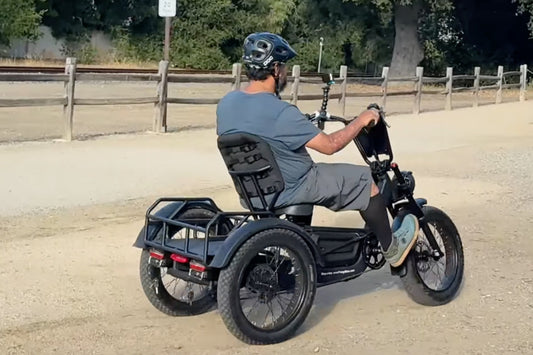 Rear view of a rider on the FlekTrike Pro All-Terrain Tilting eTrike with backrest, riding on a sandy dirt trail.