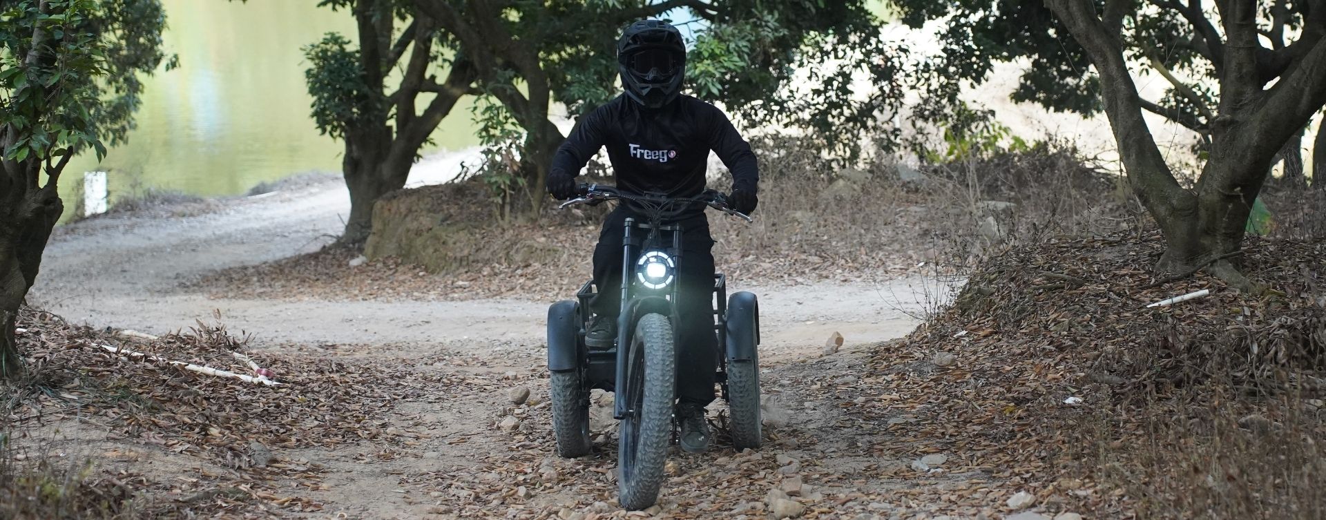 Person riding a flektrike swing on a dirt path with trees and bushes in the background.