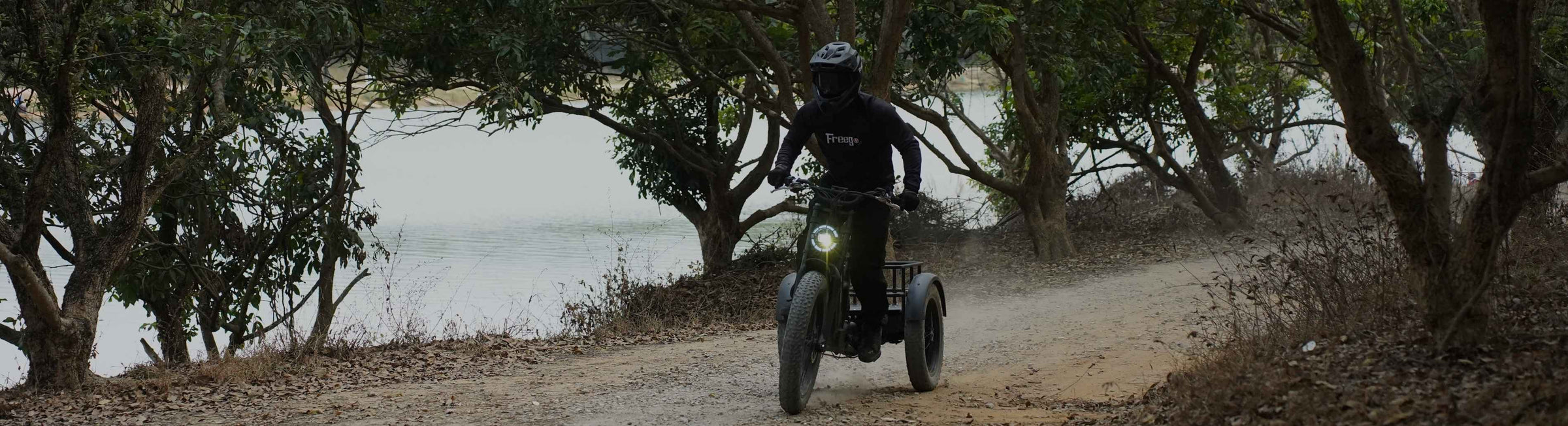 Person riding a flektrike swing on a dirt path with trees and water in the background