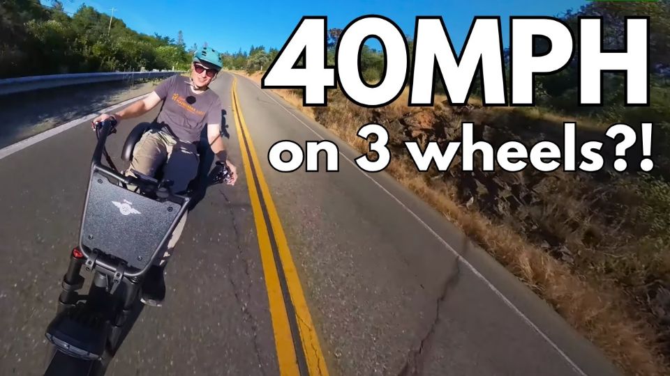 A person riding a three-wheel electric scooter on a paved road with large white text overlay reading '40MPH on 3 wheels?!'.