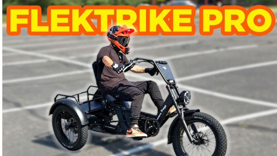 A person wearing a helmet rides a black three-wheeled electric sidecar motorcycle labeled 'FLEKTRIKE PRO' in a paved parking lot.